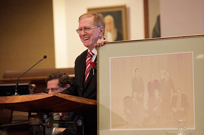 Photo: Michael Kirby at the podium, with the photograph of the original commissioners, described in the text below